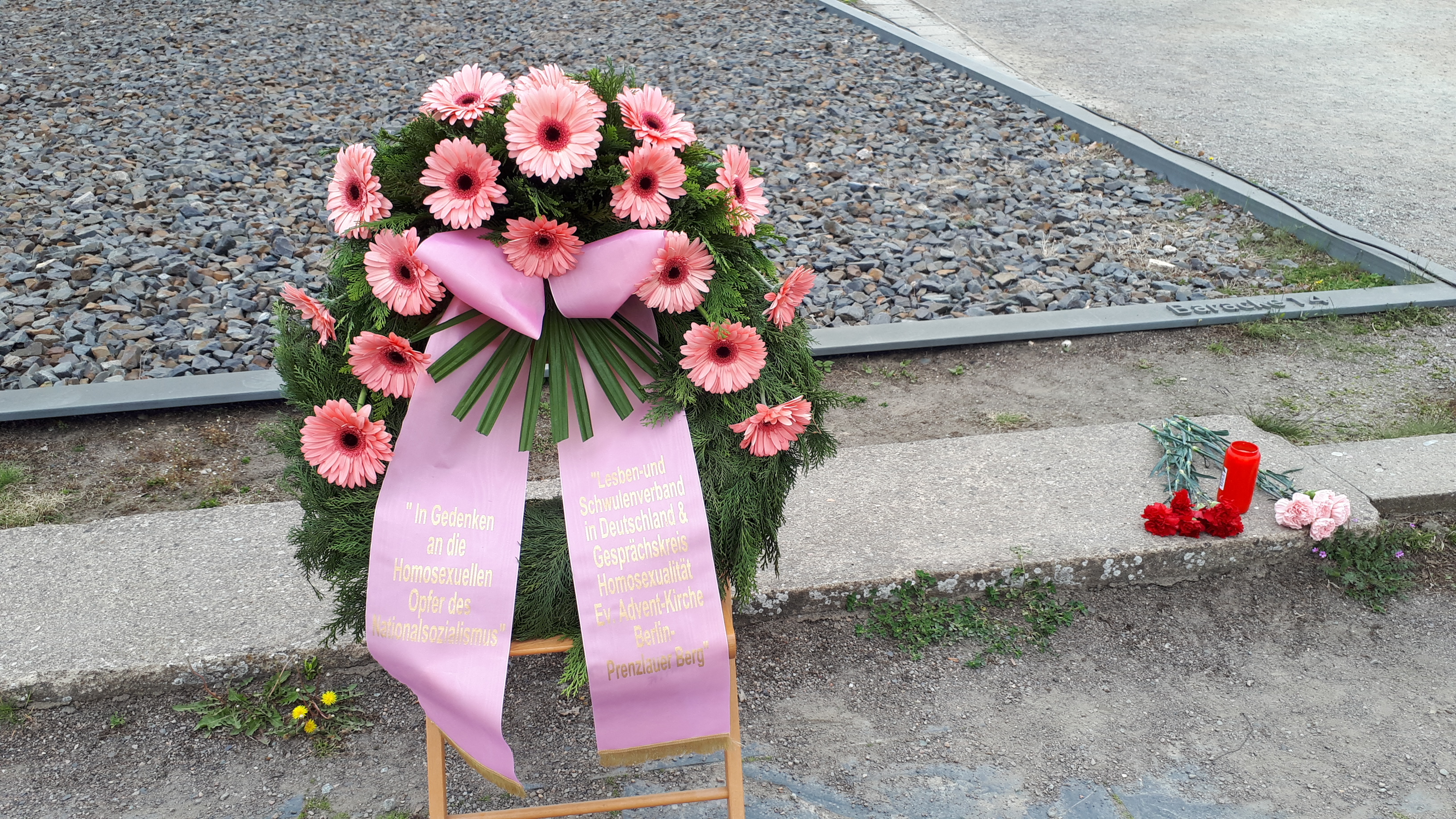 Gedenkkranz mit rosa Gerbera und Bändern auf Schotter.