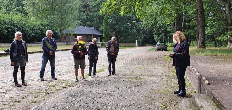 Gruppe von Menschen hört einer Frau zu, die im Freien liest.